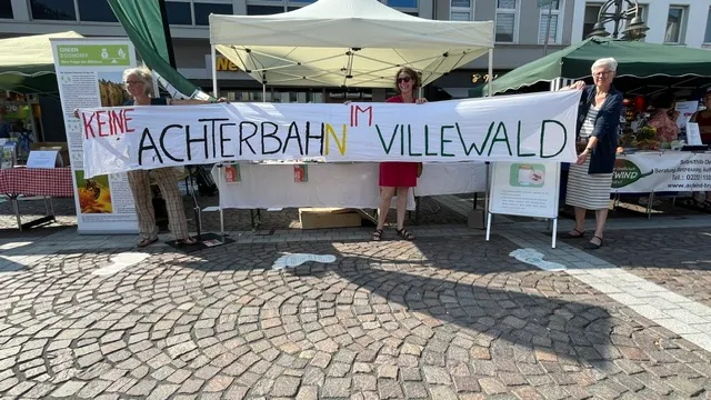 Drei Frauen halten ein Schild hoch, auf dem 'Keine Achterbahn im Villewald' steht